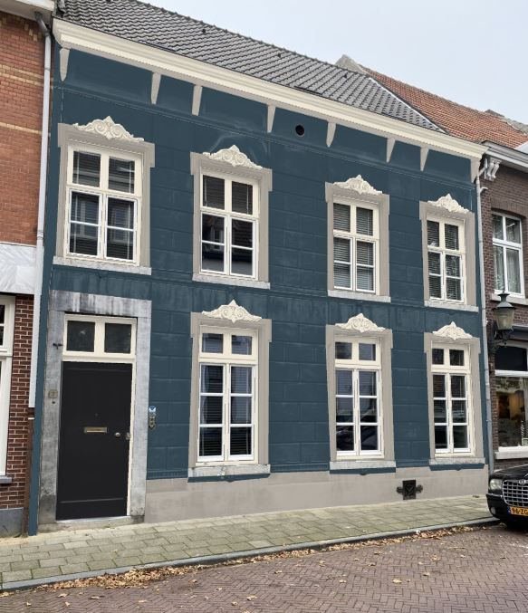 Een blauw gebouw van twee verdiepingen met witte kozijnen, sierlijsten boven elk raam en een zwarte voordeur.