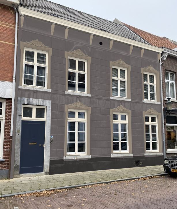 Een historisch, grijs gebouw van twee verdiepingen met een blauwe deur, wit omlijste ramen en sierlijke stenen details aan een geplaveide straat.