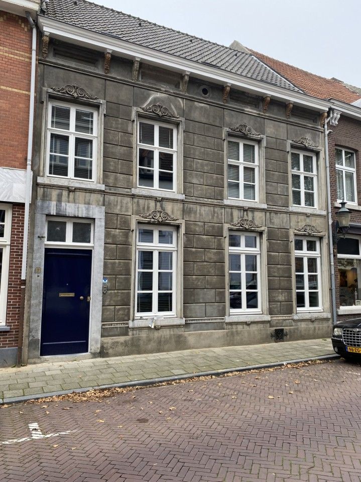 Een historisch stenen gebouw van twee verdiepingen met een blauwe deur en rechthoekige ramen, gelegen aan een straat met kinderkopjes.