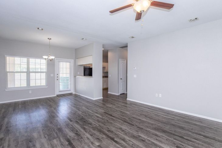 Empty living room with gray walls, wood-look flooring, and a ceiling fan.
