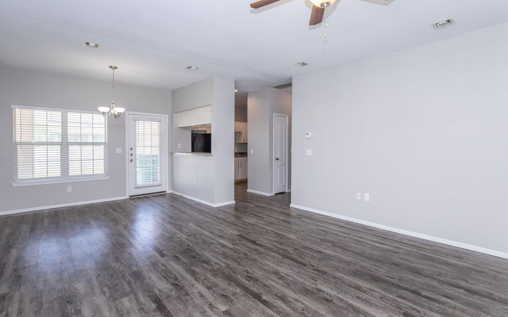 Empty living room with gray walls, wood-look flooring, and a ceiling fan.