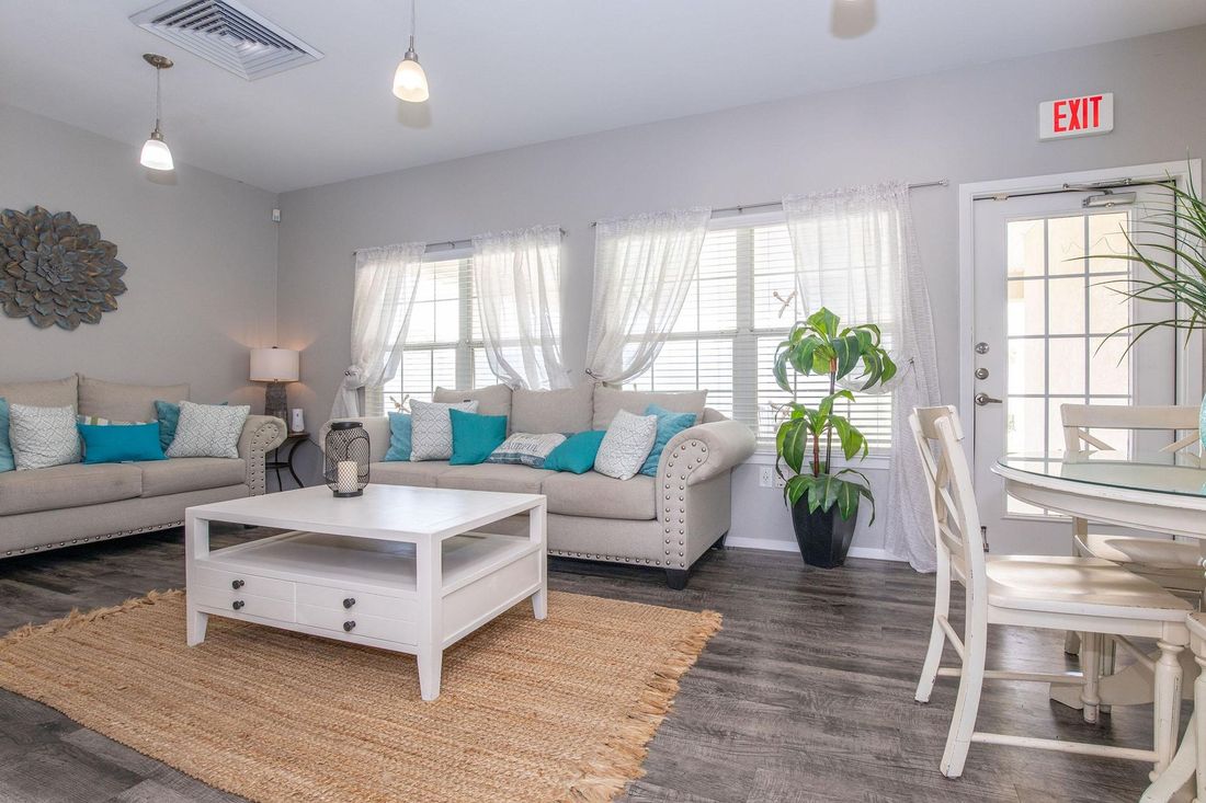 Living room with gray walls, beige sofas, turquoise pillows, white coffee table, and a round dining table.
