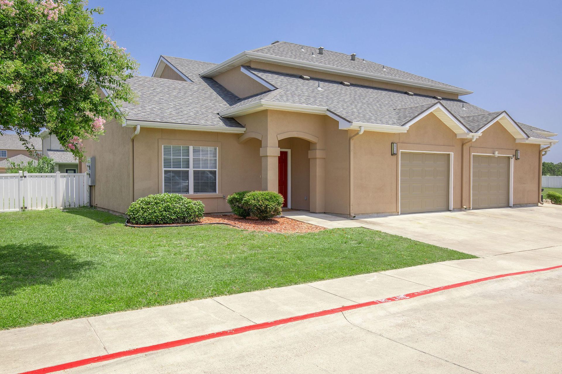 Tan house with a red front door, three garage doors, and a green lawn under a blue sky.