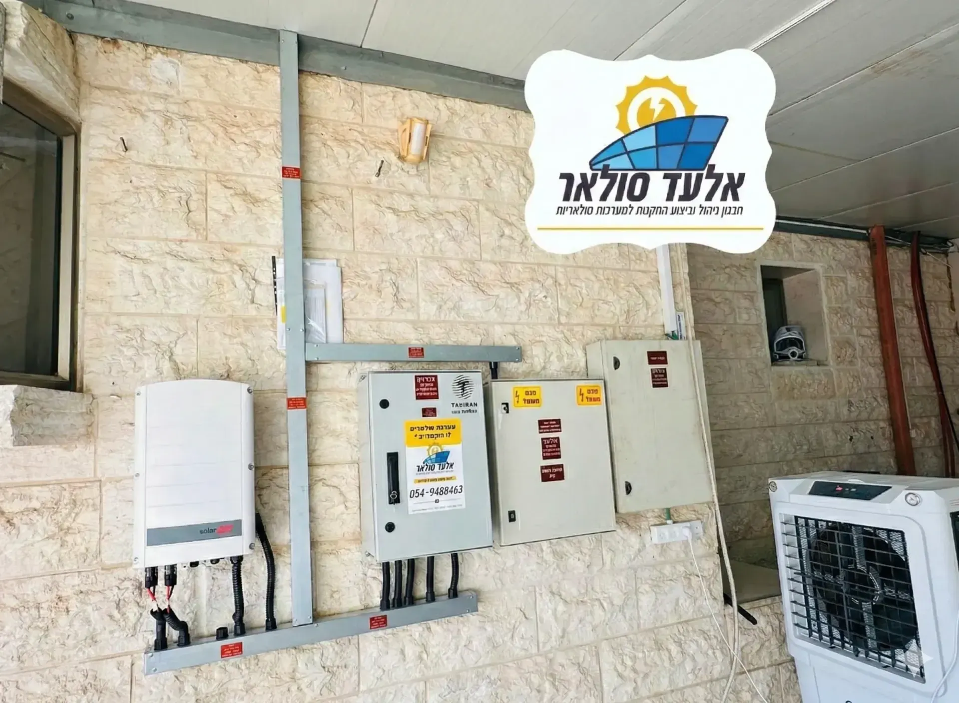 מבט אווירי על גג עם פאנלים סולאריים ולוגו עברי מעל רחוב שטוף שמש למטה.