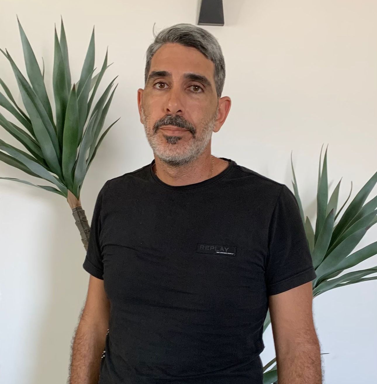 גבר בחולצה שחורה עומד מול צמח