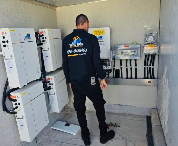 אדם במדים שחורים בודק רכיבי פאנל סולארי בתוך חדר שירות.