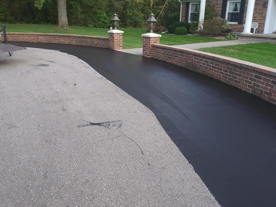 A person is spreading black paint on a concrete surface.