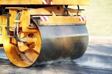 A yellow roller is rolling asphalt on a road.