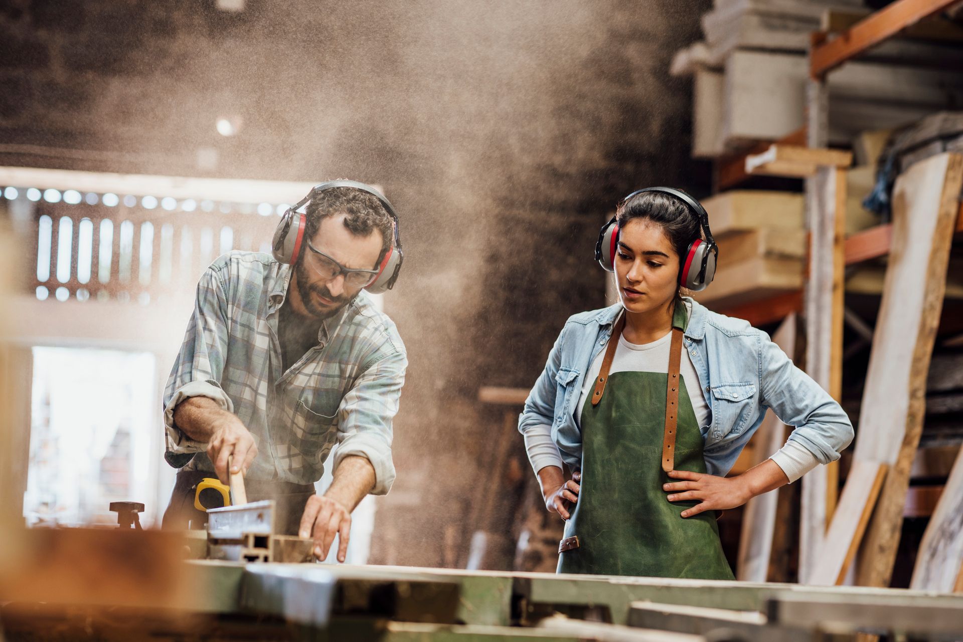 Craftsman sanding timber while woman observes in workshop during custom joinery project.