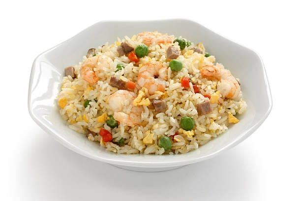 Shrimp fried rice in a white octagonal bowl, with green peas, red peppers, and scrambled egg.
