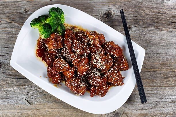 Sweet and sour sesame chicken with broccoli on a white plate, chopstick.