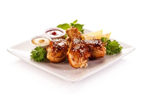 Fried chicken drumsticks with sauces, parsley, and lemon slices on a white plate.