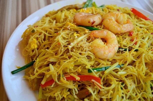 Plate of yellow Singapore noodles with shrimp and vegetables.