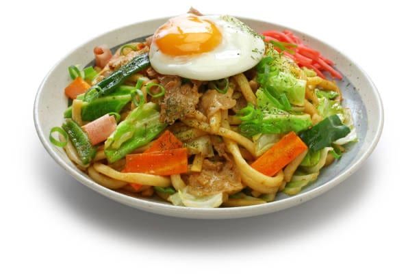 Noodles with vegetables and a fried egg in a white bowl, garnished with pickled ginger.
