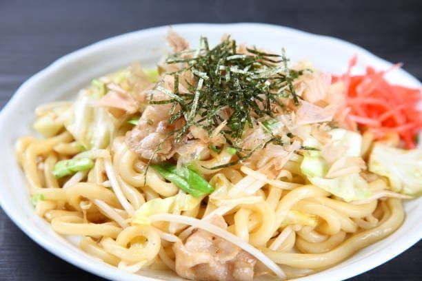 Udon noodles with cabbage, pork, and garnishes in a white bowl.