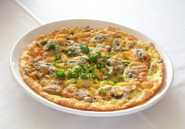 Oyster omelet on a white plate, garnished with green onions, golden brown edges.