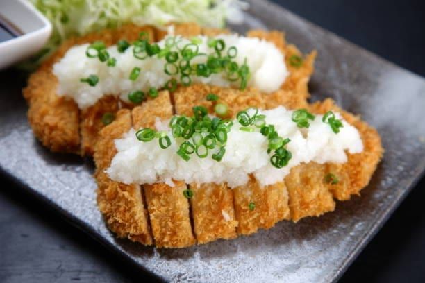 Crispy fried pork cutlets topped with grated daikon radish and scallions on a black plate.