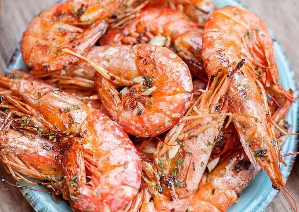 Pile of cooked shrimp on a blue plate, seasoned with herbs and garlic.