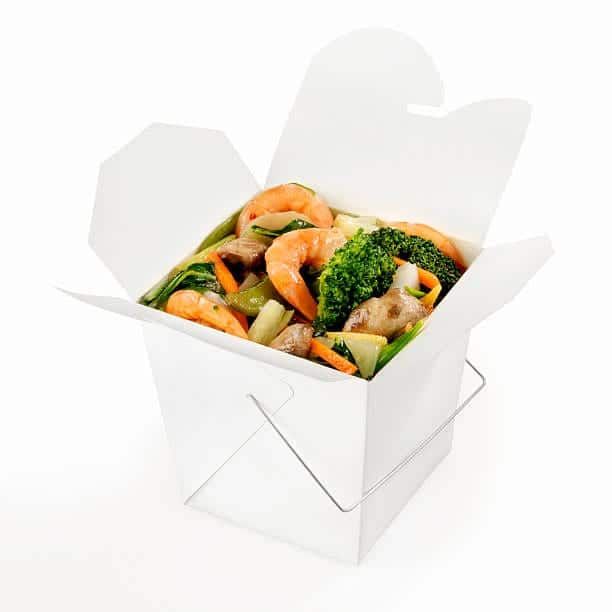Shrimp and vegetable stir-fry in an open white takeout box with a wire handle; white background.