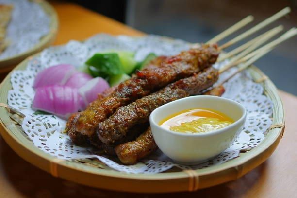 Grilled meat skewers with sauce, onions, and cucumber on a wicker plate.