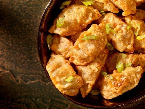 Golden fried dumplings in a dark bowl, sprinkled with green onions.
