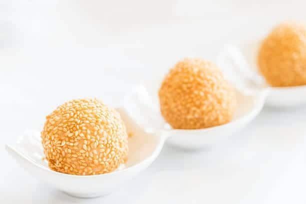 Three golden sesame balls in white serving dishes.