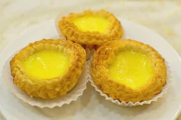 Three egg tarts with golden, custard-filled centers on a white plate.