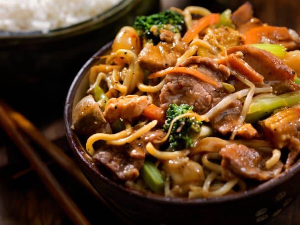 Close-up of a bowl of stir-fry with noodles, meat, and vegetables.