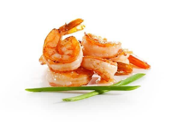 Cooked shrimp with green onion garnish on a white surface.