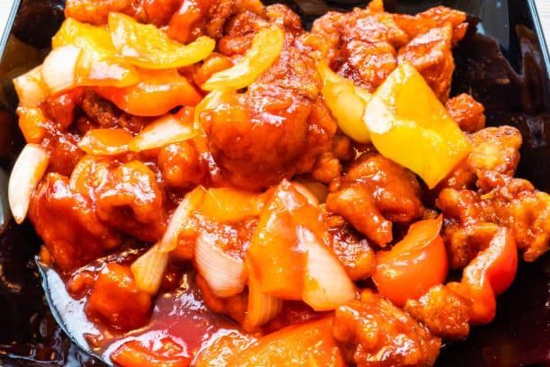 Sweet and sour chicken with bell peppers and onions in a red sauce.