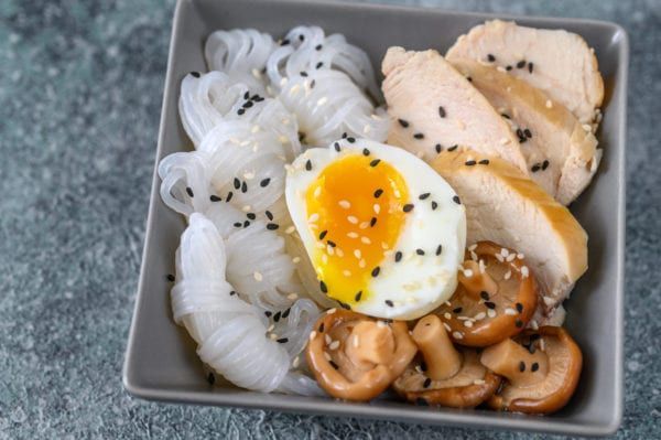 Bowl of noodles, chicken, egg, and mushrooms, sprinkled with sesame seeds.