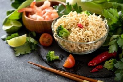Bowl of noodles, shrimp, and vegetables with chopsticks.