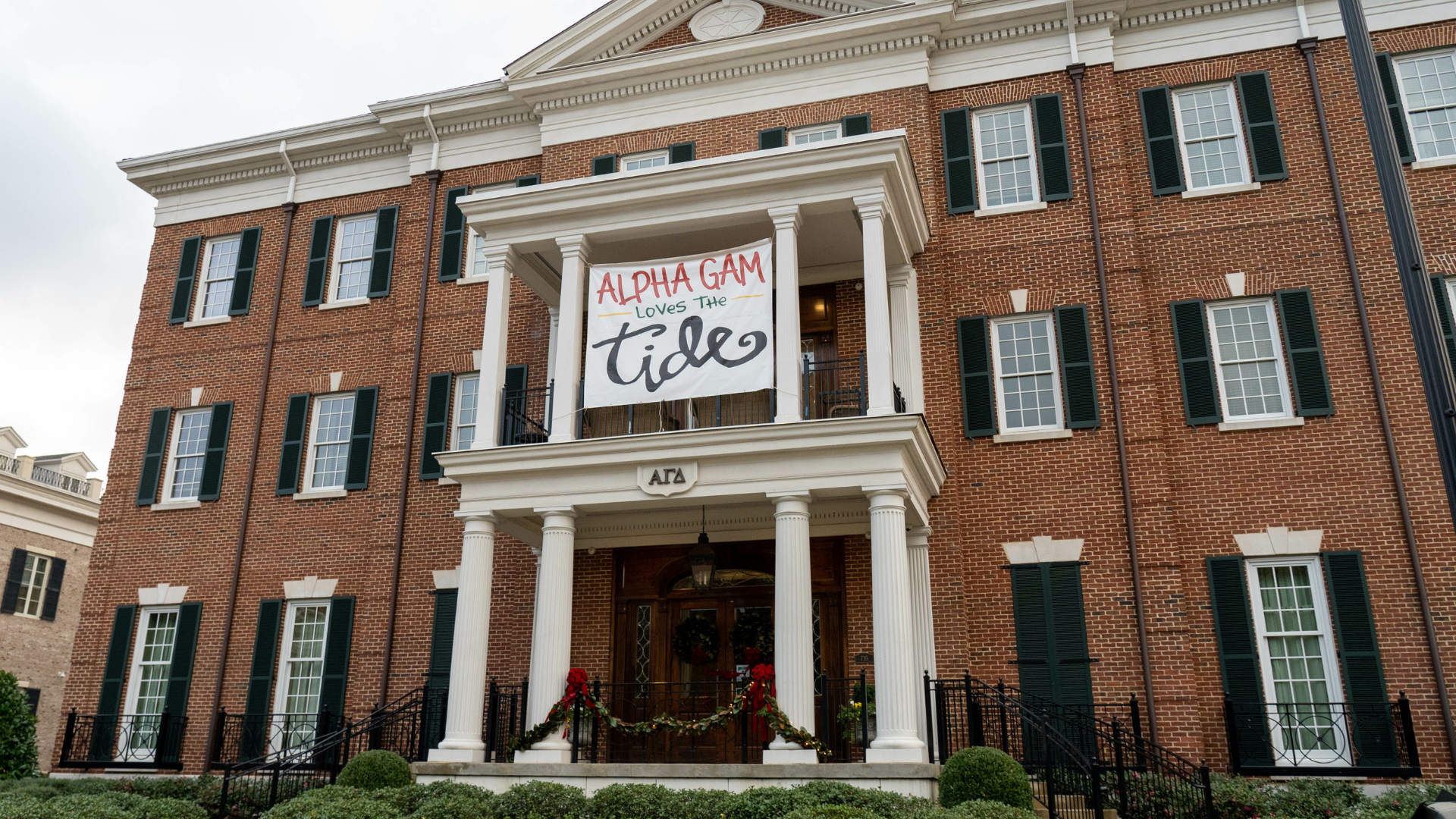 A large brick building with a sign on the porch that says Alpha Gam loves the tide