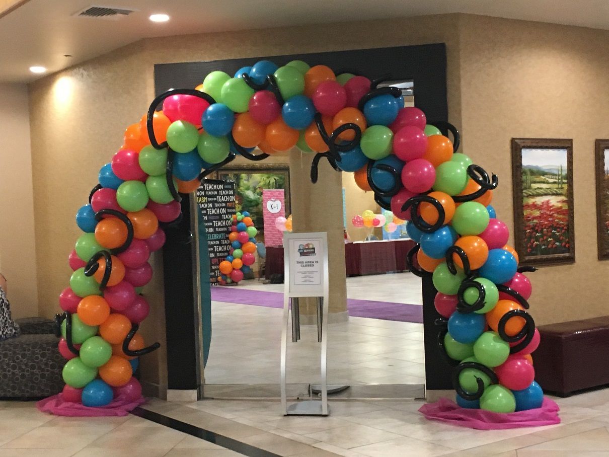 A colorful balloon arch is surrounding a doorway in a room.