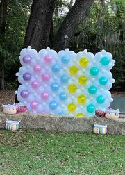A wall made of balloons is sitting on top of a lush green field.