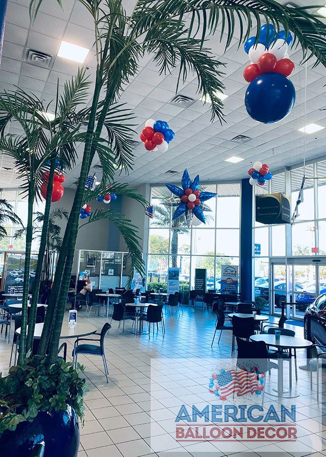 A car dealership is decorated with red , white and blue balloons.