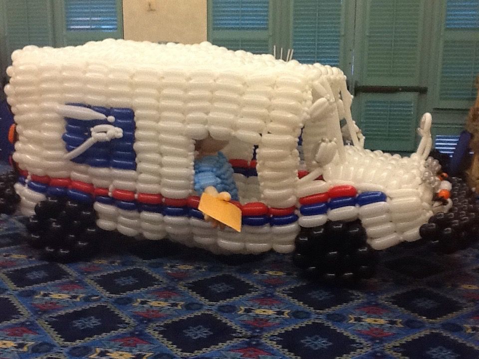 A mail truck made out of balloons is sitting on a blue rug