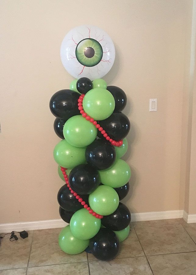 A balloon tower with green and black balloons and an eye on top.