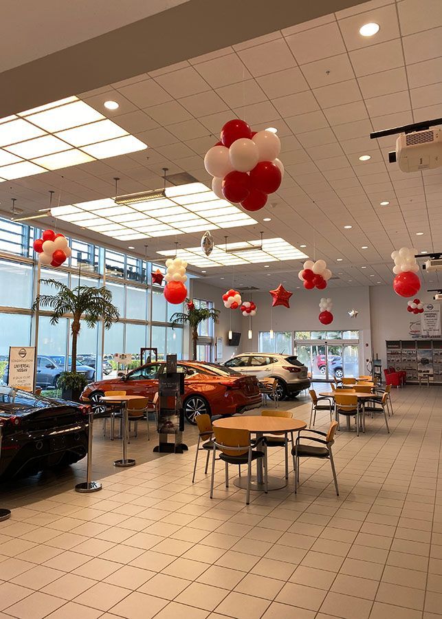 A car dealership with tables and chairs and balloons hanging from the ceiling.