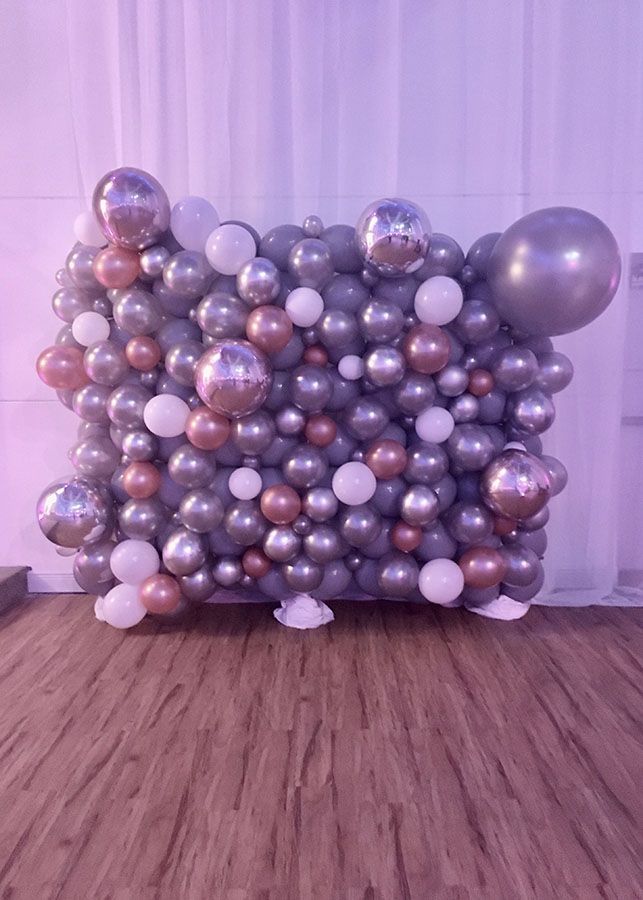 A wall of balloons on a wooden floor in a room.