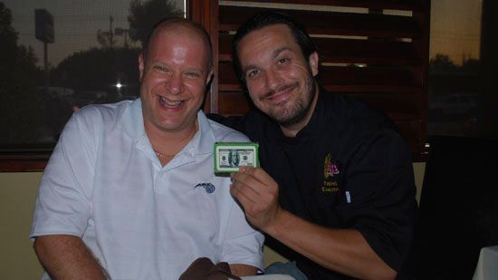 Two men posing for a picture with one holding a card that says alex