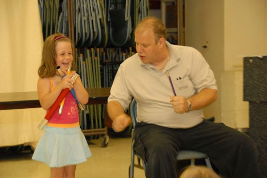 A little girl singing into a microphone next to a man in a wheelchair