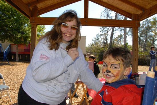 A woman paints a child 's face like a tiger