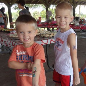 Two young boys are posing for a picture and one has a tattoo on his arm that says scorpion