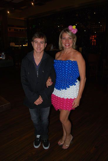 A man and a woman are posing for a picture . the woman is wearing a dress made of balloons.