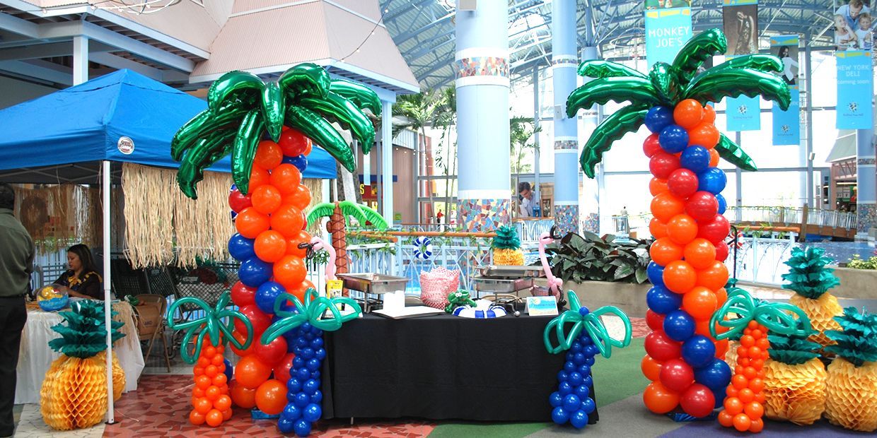 A table is decorated with balloons in the shape of palm trees and pineapples.