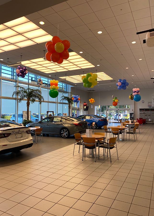 A car dealership with tables and chairs and balloons hanging from the ceiling.
