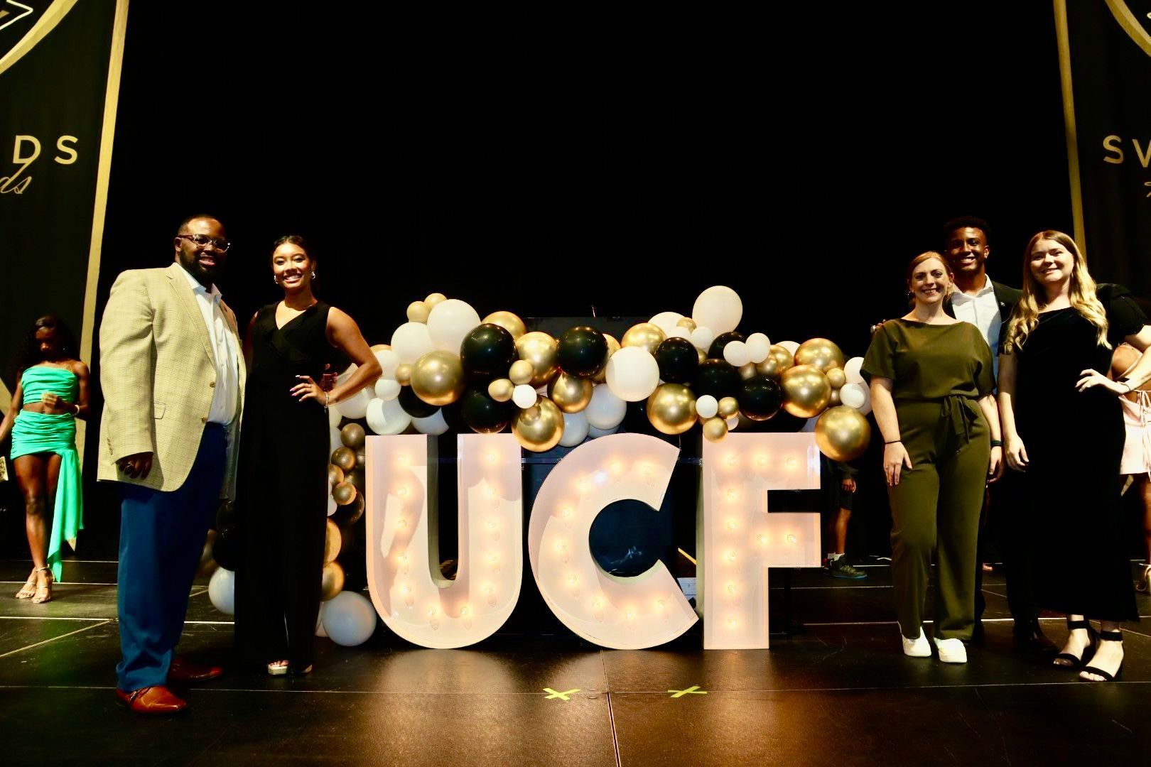 A group of people are standing in front of a large sign that says ucf.