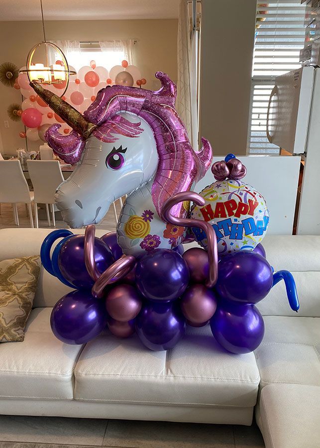 A unicorn balloon is sitting on top of purple balloons on a couch.