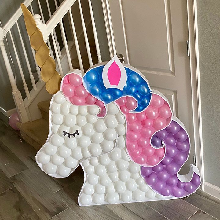 A unicorn made of balloons is sitting on the floor next to a staircase.